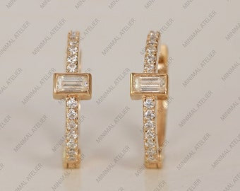 May include: A pair of gold hoop earrings with a single baguette diamond set in each hoop. The hoops are lined with small round diamonds.