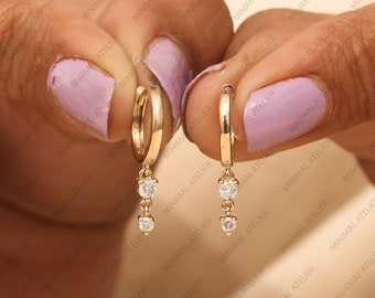 May include: A pair of gold hoop earrings with a dangling chain of three small diamonds.