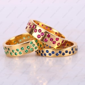 May include: Three gold rings with different colored gemstones. The top ring has red gemstones, the middle ring has green gemstones, and the bottom ring has blue gemstones.