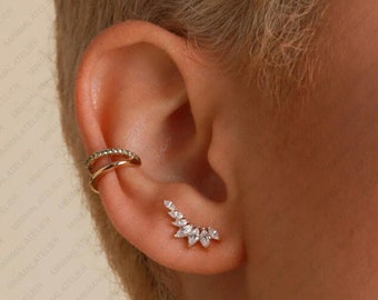 May include: A pair of gold ear cuffs with a row of small clear stones. The ear cuff on the lower ear is a curved design with a row of clear stones.
