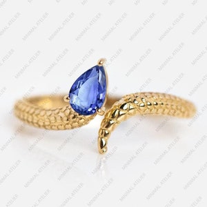 May include: A gold ring with a blue pear-shaped gemstone set in the center. The ring is designed to look like a snake with a textured body.