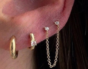 May include: Gold hoop earrings with a small diamond stud and a chain connecting two diamond studs in the upper ear.