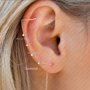 Puede incluir: Un pendiente de cadena de oro con pequeños detalles de diamantes. La cadena cuelga del lóbulo de la oreja y termina en un pequeño diamante. El pendiente tiene un diseño minimalista y es perfecto para el uso diario.