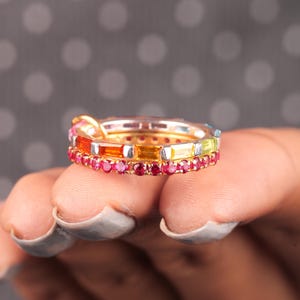 May include: A set of three gold rings with colorful gemstones. The rings are stacked on top of each other and feature a variety of colors, including red, orange, yellow, green, blue, and purple.