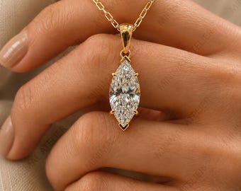 May include: A gold necklace featuring a marquise-cut clear gemstone pendant held in a four-prong setting. The pendant is suspended from a delicate gold chain with rectangular links, showcasing a faceted stone that reflects light from its center.
