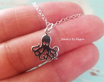 Puede incluir: Un collar de plata con un delicado colgante de pulpo. El collar está en una cadena y se sostiene en una mano.