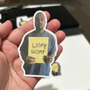 Può includere: Un adesivo di una persona che tiene un post-it giallo con la parola "WOMP" scritta due volte.