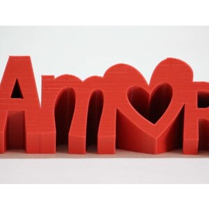 May include: Red 3D plastic letters spelling "Amor" with a heart cutout in the "O".