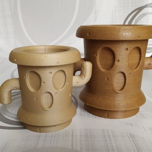 Peut inclure: Deux pots de fleurs en forme de cactus imprimés en 3D de couleur marron avec un visage de dessin animé. Le plus grand pot est plus haut et a une base plus large. Le plus petit pot est plus court et a une base plus étroite.