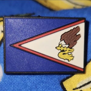 May include: A blue, white, and red flag with a stylized eagle design. The flag is made of a rubber-like material and has a black border.