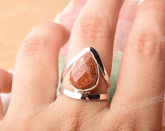 May include: A silver ring with a teardrop-shaped red-brown gemstone. The ring has a delicate, open design.