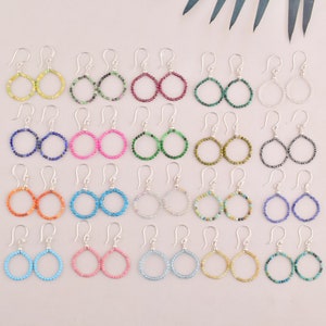 May include: Twenty-four pairs of silver hoop earrings with different colored gemstone beads. The earrings are arranged in four rows of six pairs.