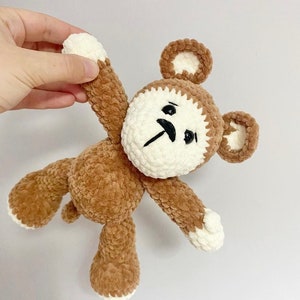 May include: A brown crocheted plush toy bear with white accents on the ears, paws, and face. The bear has a white face with black eyes and a black moustache.