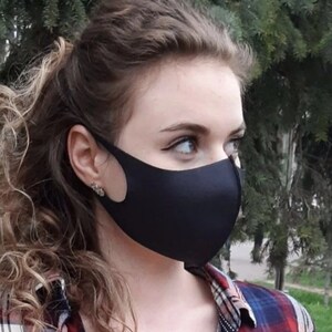 May include: A woman with curly brown hair is wearing a black face mask and a red and blue plaid shirt.