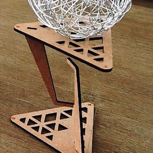 May include: A wooden triangular stand with a geometric pattern holds a white string ball light.