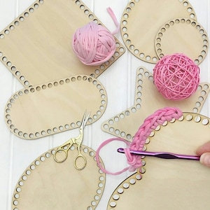 May include: A set of wooden embroidery hoops in various shapes, including a square, circle, star, heart, and oval. The hoops are made of natural wood and have a light brown color. Pink yarn is wrapped around some of the hoops, and a crochet hook is visible in the image.