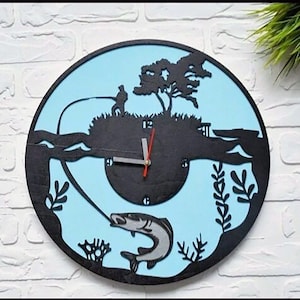 May include: A black and blue wooden clock with a silhouette of a fisherman on a lake, a tree, and a fish jumping out of the water. The clock face is black with white numbers and hands.