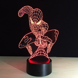 May include: Red 3D LED night light featuring a Spiderman design. The light is on a black base with a red light shining through the Spiderman design.