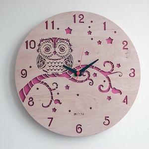 May include: A round wooden wall clock featuring a laser-cut owl perched on a branch. The clock face is light-colored with a pink branch and star accents. Black clock hands and a red second hand complete the design. The clock is a decorative item.
