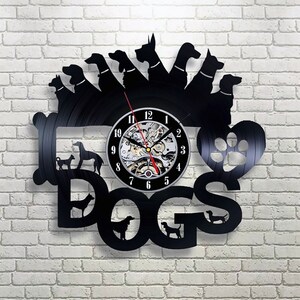 Könnte beinhalten: Schwarze Schallplattenuhr mit einem Pfotenabdruck-Design und dem Wort "DOGS" in großen Buchstaben. Das Zifferblatt der Uhr ist von Silhouetten verschiedener Hunderassen umgeben.