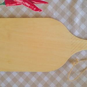 May include: A light brown wooden cutting board with a long handle and a string attached to the handle. The board is oval shaped and has a smooth surface.