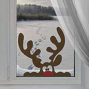 May include: A brown reindeer window cling with large antlers, a red nose, and wide eyes. The cling is placed on a window overlooking a snowy landscape with a forest in the distance. A white curtain is visible.