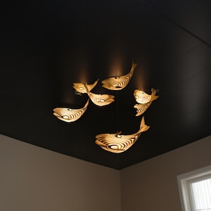 May include: A ceiling light fixture with a modern design featuring multiple fish-shaped lights. The lights are made of a light-colored material and are illuminated with warm white light.