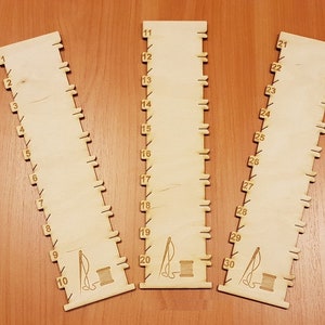 以下が含まれることがあります： 1から30までの数字が印刷された木製の定規が3本。各定規の下部には、針と糸の小さなイラストが描かれています。