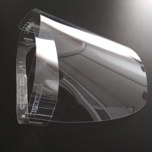 May include: A clear plastic face shield with a headband. The shield is curved and has a clear plastic band around the top.