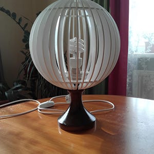 May include: A white globe lamp with a wooden frame and a black base. The lamp has a white light bulb inside.