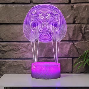 May include: A purple 3D printed night light shaped like a walrus head. The light is on a white base with a cracked glass effect.