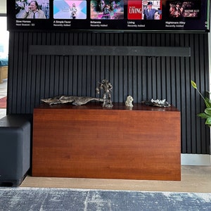 May include: A black television screen showing the film "Oppenheimer" with a fiery explosion in the background. Below the screen is a wooden entertainment unit with a black speaker and a decorative statue.