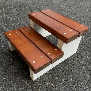 May include: A two-step wooden stool with a white base and brown wooden steps. The steps are secured with silver screws.