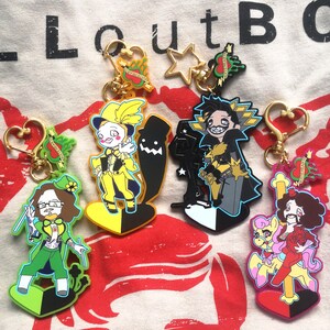 May include: Collection of character keychains with gold-colored hardware. The keychains feature various cartoon figures in vibrant colors, including yellow, green, black, and pink. Some keychains have heart-shaped and star-shaped clasps.