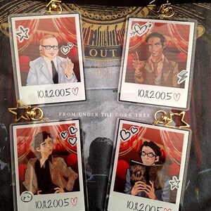 Peut inclure: Quatre porte-cl&eacute;s rectangulaires en acrylique avec des portraits illustr&eacute;s style polaro&iuml;d. Chaque porte-cl&eacute;s poss&egrave;de un fermoir en forme d'&eacute;toile dor&eacute;e et affiche la date 10.11.2005 avec un c&oelig;ur. Les illustrations montrent des personnages et des rideaux rouges.