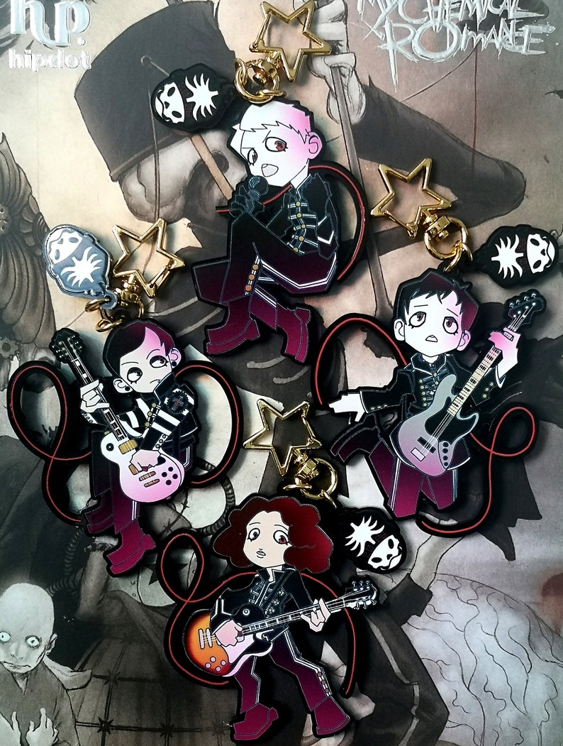 May include: A selection of enamel keyrings featuring cartoon illustrations of band members. Each keyring depicts a musician with a guitar or microphone, in black and burgundy outfits. Additional charms include star shapes and a skull design.