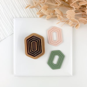 Puede incluir: Conjunto de tres cortadores de galletas geométricos en marrón, rosa y verde. Los cortadores tienen forma de hexágono con esquinas redondeadas.