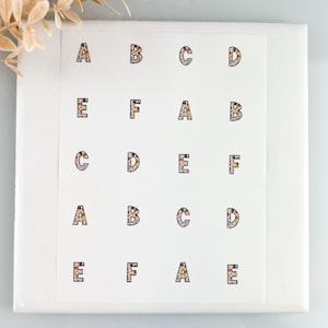 May include: A sheet of alphabet stickers, each letter from A to F, is displayed. The letters are in a floral pattern with a white background. The stickers are arranged in rows and columns on a white square.