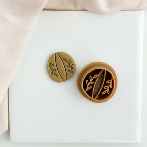 May include: Two brown plastic cookie cutters with a leaf design. The cutter on the left is solid and the cutter on the right is open.