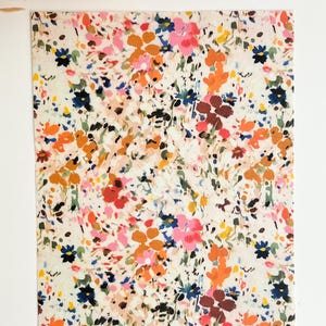 May include: A white background with a floral pattern in shades of pink, orange, yellow, blue, and green. The flowers are abstract and have a watercolor effect.