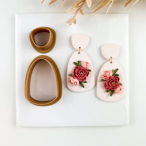 May include: A set of polymer clay earring components and two finished earrings. The earrings are light pink with a floral design of red and pink roses. The clay cutters are brown.