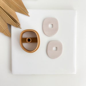 May include: Three ceramic clay shapes, two are light pink with a textured surface and a small hole in the center, the other is a brown clay shape with a hole in the center.