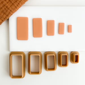 May include: Set of six brown plastic rectangle-shaped cookie cutters of varying sizes on a white surface.