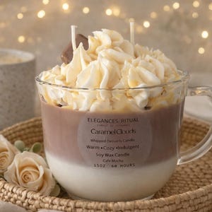 May include: A clear glass mug-shaped candle filled with layers of white and brown wax, topped with whipped cream-like wax and a chocolate accent. The candle sits on a woven tray with roses. The label reads "Caramel Clouds" and "Cafe Mocha".