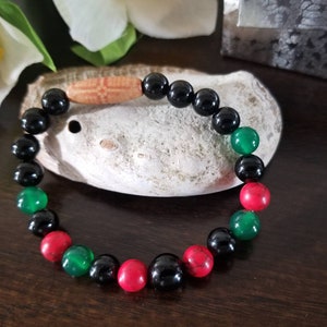 May include: A beaded bracelet with black, green, and red beads. The bracelet has a wooden bead with a carved design.