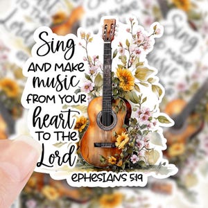 May include: A sticker featuring a brown acoustic guitar with floral accents and the text "Sing and make music from your heart to the Lord, Ephesians 5:19." The sticker has a white border and is held by a hand.