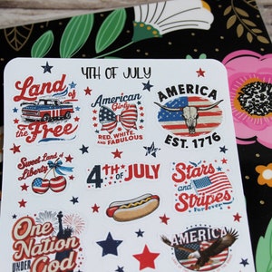 May include: A sheet of stickers with patriotic designs for the 4th of July. The stickers feature images of a truck, a bow, a steer skull, a hot dog, the American flag, and the Statue of Liberty. Text includes "Land of the Free", "America", and "Stars and Stripes".