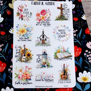 May include: A sticker sheet with the words "Faithful Words" and various floral and religious designs. The stickers include phrases like "God is Love," "Protected by His Grace," and "Let us worship together." The sheet is on a floral patterned background.