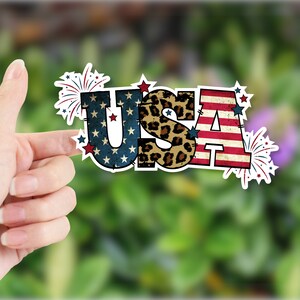 May include: A sticker with the word "USA" in large, bold letters. The letters are decorated with a red, white, and blue American flag pattern, a leopard print pattern, and fireworks.