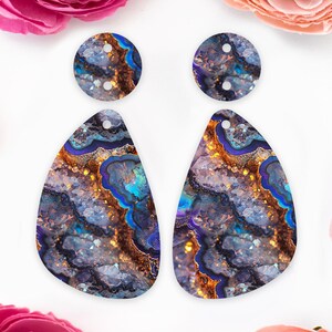 May include: A pair of dangle earrings with a teardrop-shaped design. The earrings feature a blue, purple and gold agate pattern with a sparkly finish.
